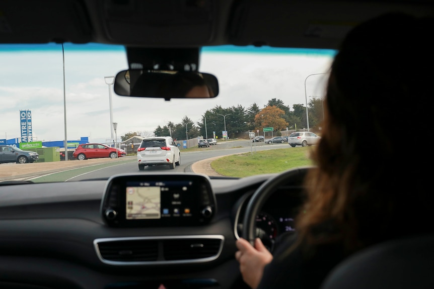 A woman is seen from behind driving a car around a roundabout