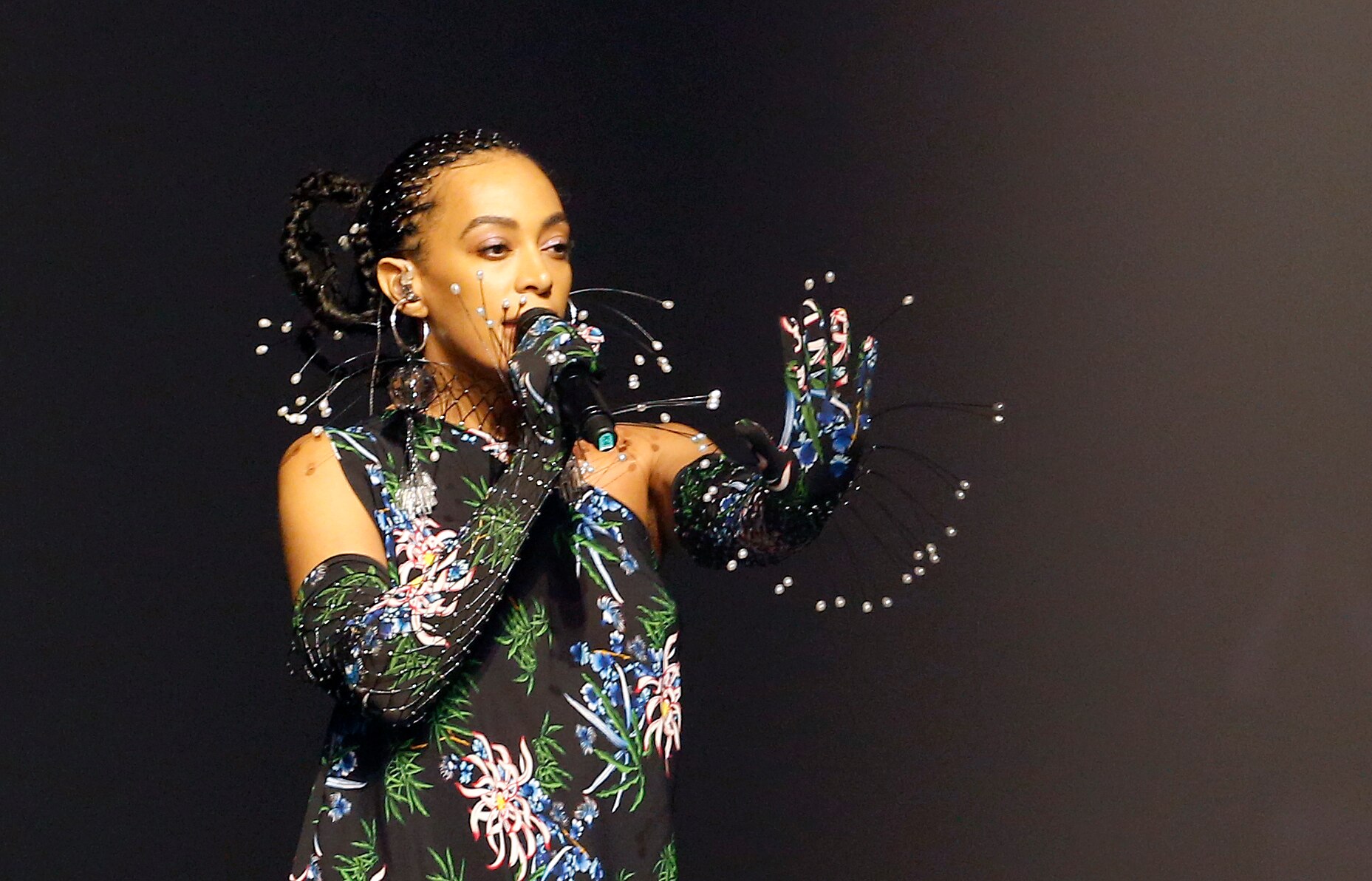 Solange holds a hand out while singing in an elaborate patterned look with 3D elements.