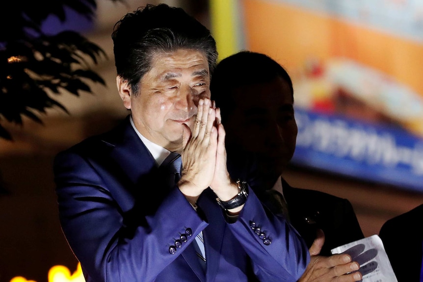 Shinzo Abe gestures with hands in front of face at an election campaign rally