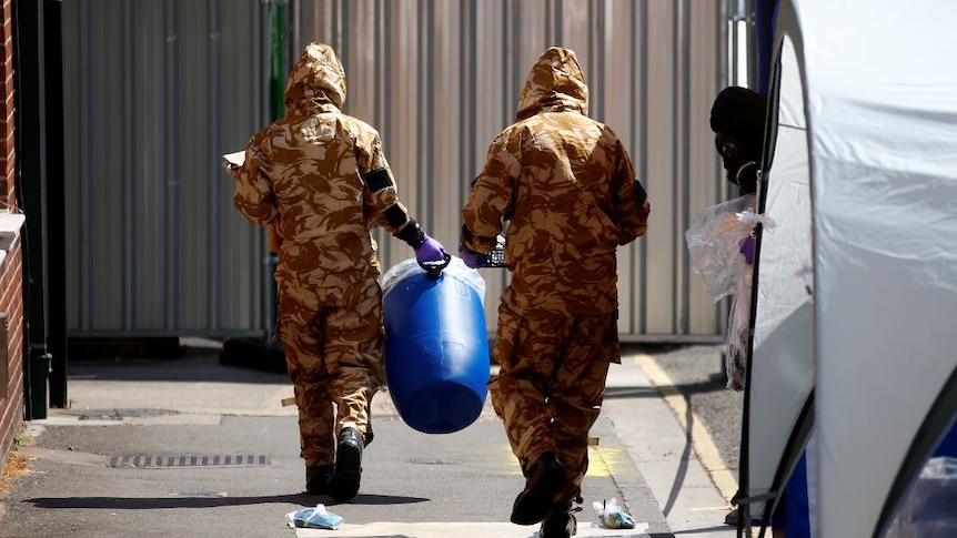 Forensic investigators wearing protective suits enter the rear of John Baker House.