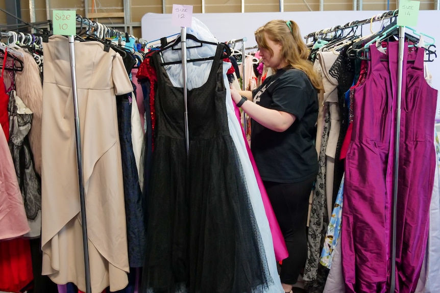 Three racks of dresses with a girl with long blond hair checking the middle one. 