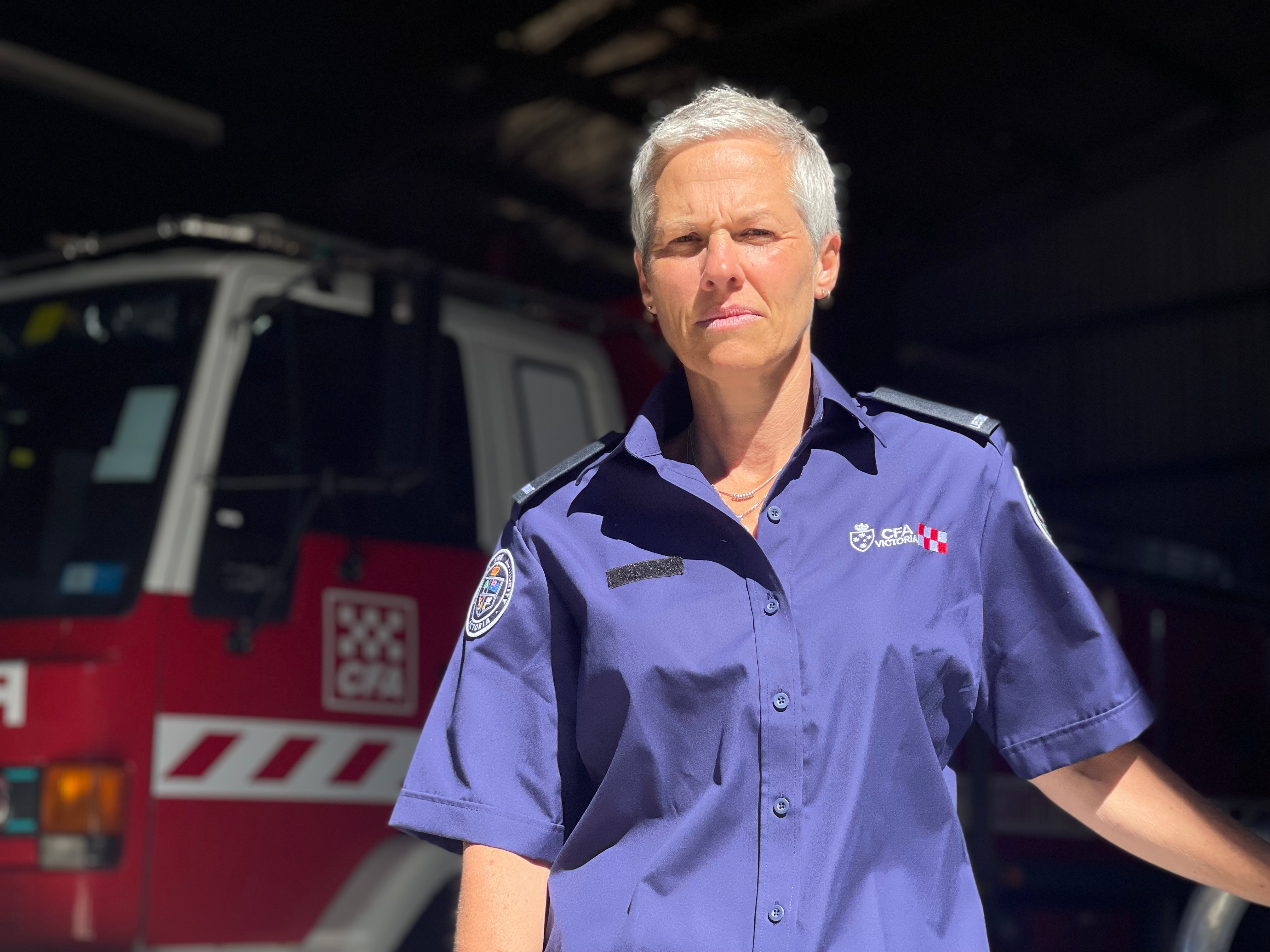 CFA volunteer Bec Closter standing in front of a blurred CFA truck, she is wearing her CFA volunteer uniform. 