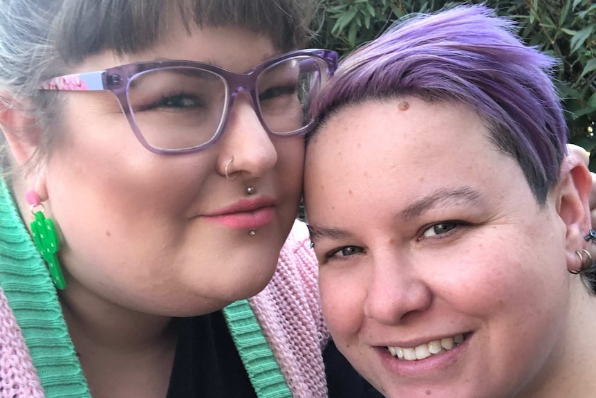 A woman in glasses hugs a woman with purple dyed hair