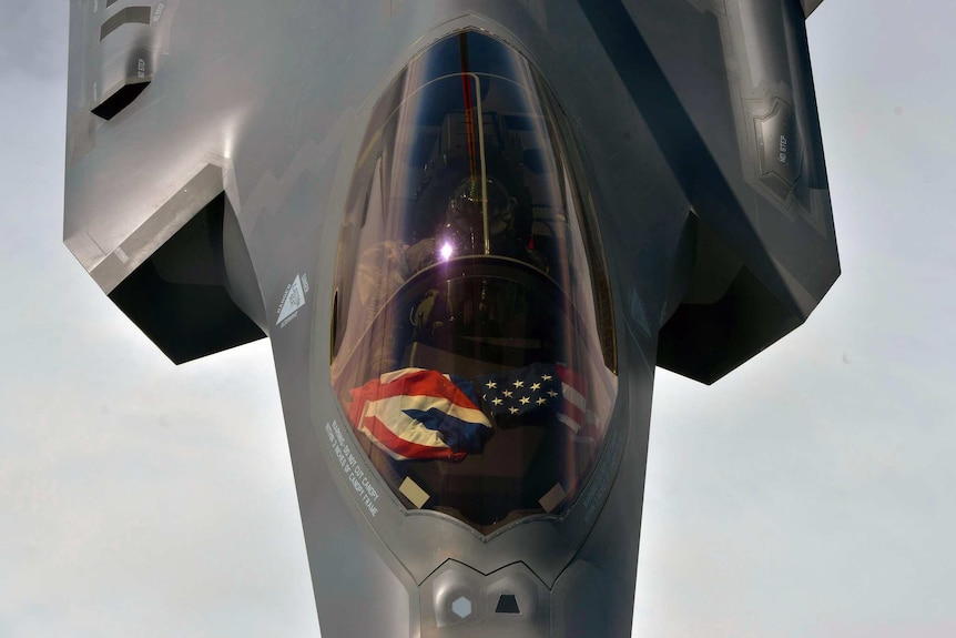 In mid air, you look down onto the top of a cockpit of the F-35A fighter jet with British and American flags on the dashboard.