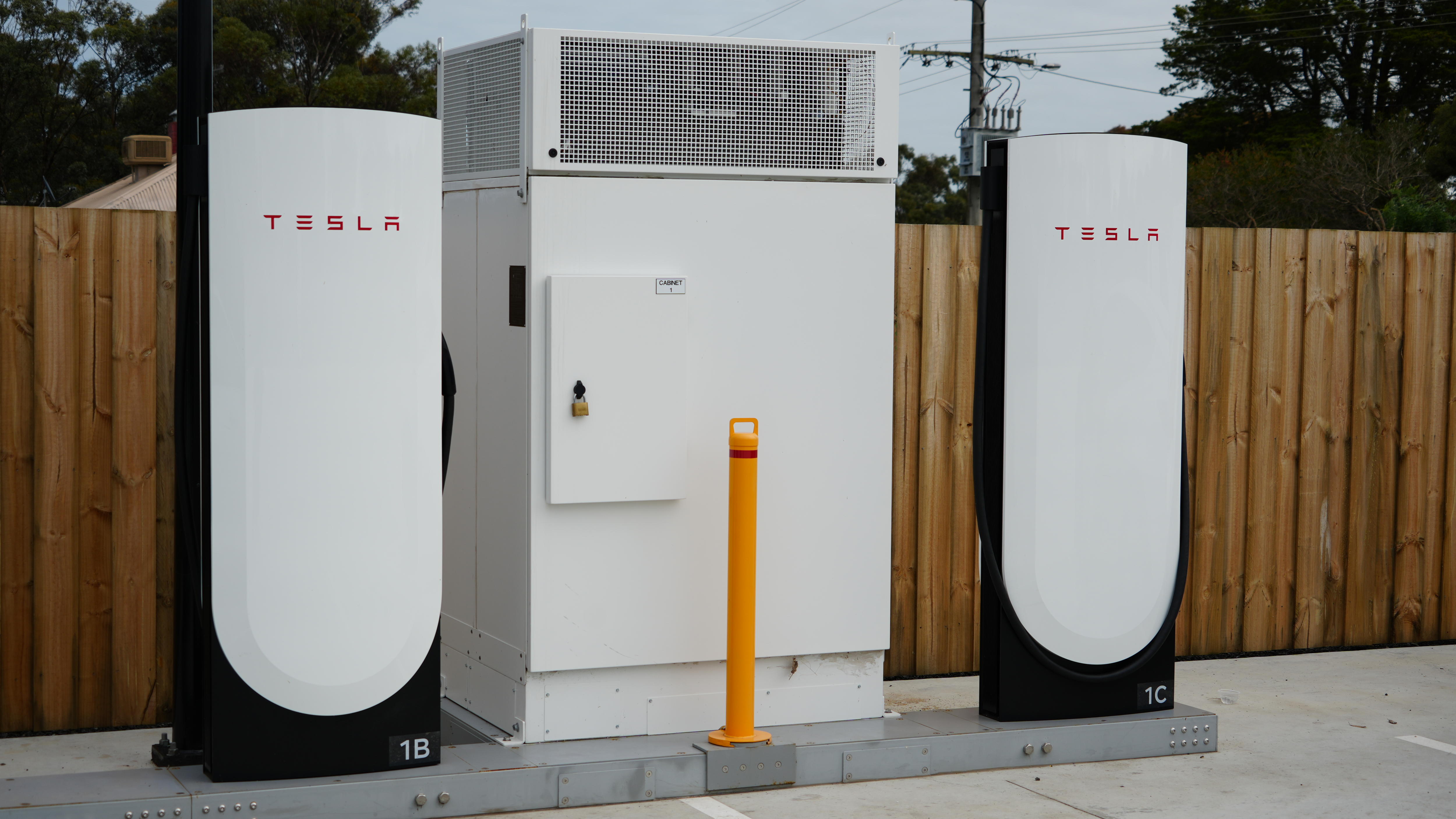 A large metal box stands between two Tesla Supercharger stations.