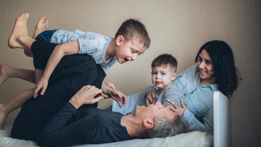 Man and woman and their two children play on the bed in a story about having the vasectomy talk.