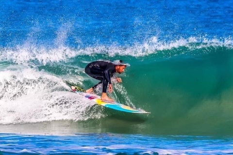 Man riding a long board tucks his head under a wave. 