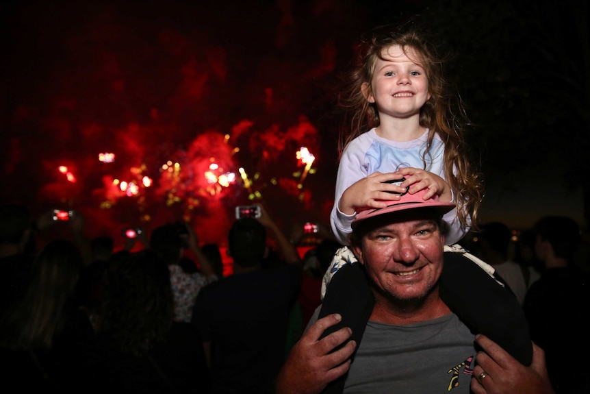 Reece Britton stands with his daughter Chevelle on his shoulders in Langley Park with the Skyworks fireworks show behind them.