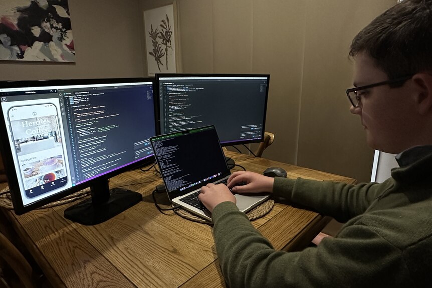 Teenage boy sitting at a desk with two large computer monitors on it