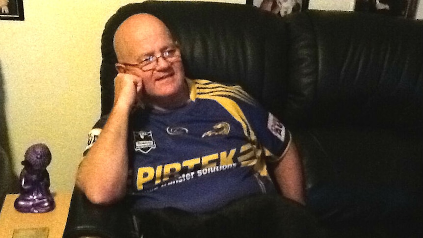 A man in a Parramatta Eels shirt sits on a couch