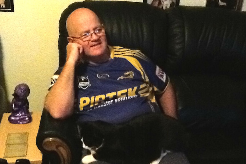 A man in a Parramatta Eels shirt sits on a couch