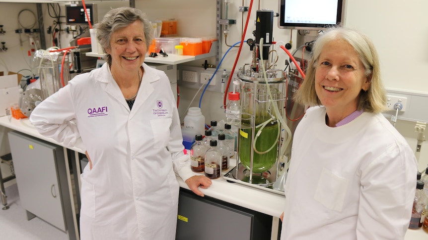 Two women in lab coats in front of scientific equipment 