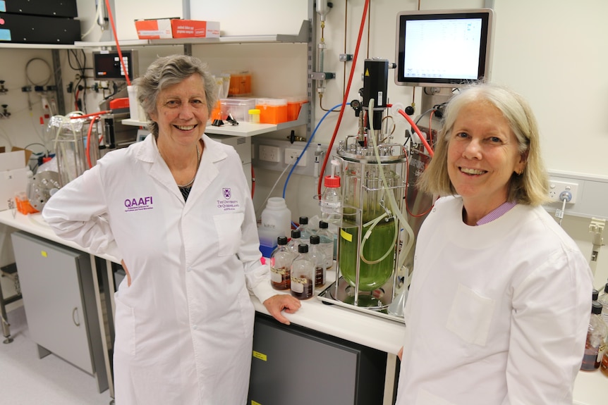 Two women in lab coats in front of scientific equipment 