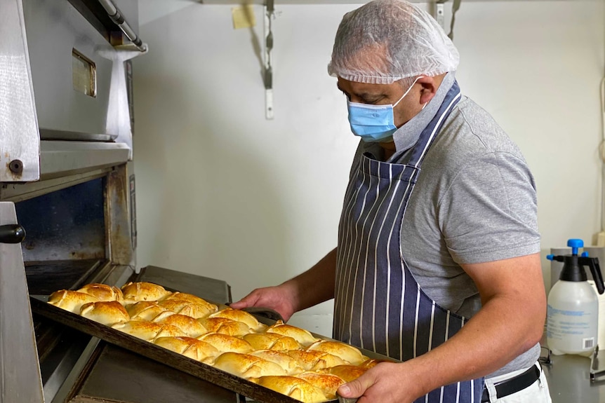 A male baker pulls a tray of pastries out of an oven.