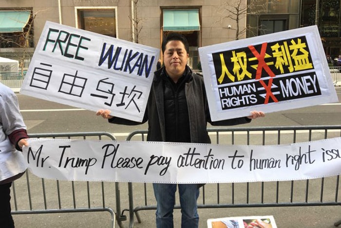A man holds up signs on the road "Free Wukan" and "Trump please pay attention to human right issues"
