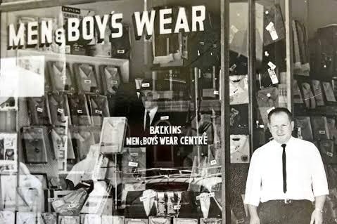 Old black and white photo with man standing out the front of a clothing store