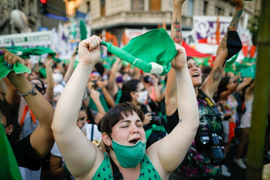 A woman holds up a green flag as she is surrounded by other women holding up flags.