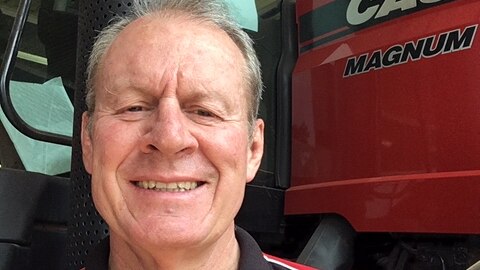 A man smiles by the side of a large tractor.