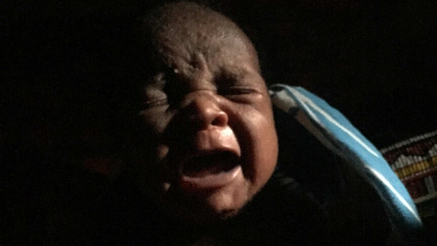 Baby Simaloi cries in the darkness of her home.
