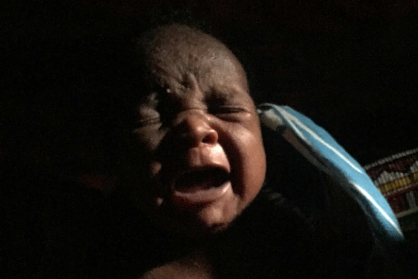 Baby Simaloi cries in the darkness of her home.