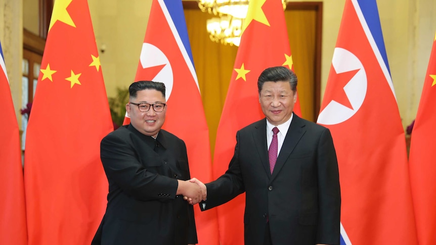 Chinese President Xi Jinping and North Korean leader Kim Jong-un shake hands in front of their national flags.