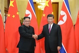 Chinese President Xi Jinping and North Korean leader Kim Jong-un shake hands in front of their national flags.