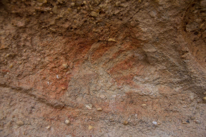 A white hand print outlined in orange-red ochre on a rock face