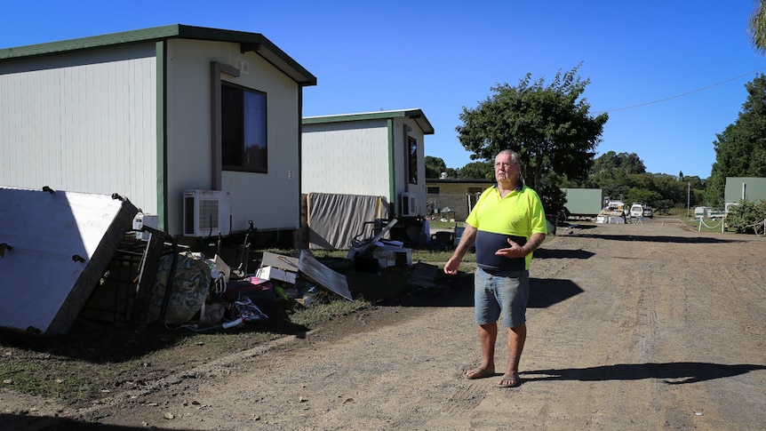 Graeme Bolton stands next to flood-damaged cabins