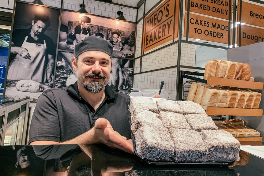 A man holds a tray of lamingtons at the counter of a bakery
