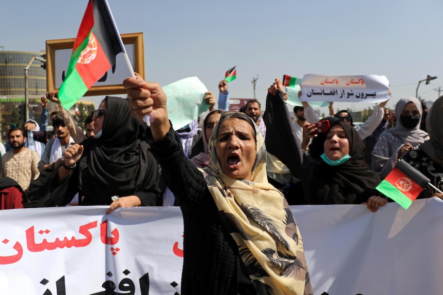 A woman wearing a headscarf waves a flag in front of a banner.