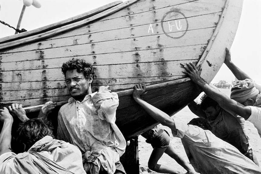 A Rohingya man strains under the weight of his heavy boat as he pushes it on to shore.