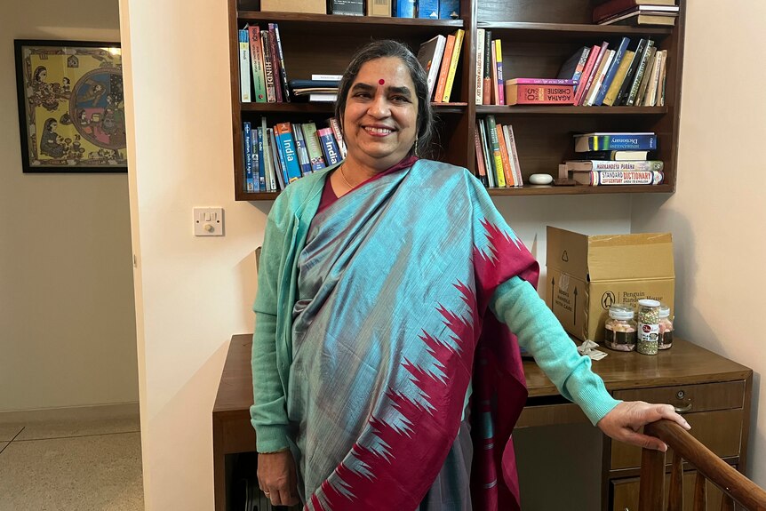 A woman in traditional Indian dress stands in front of a bookcase smiling. 