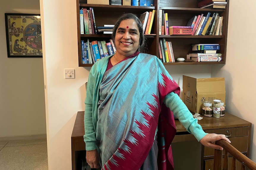 A woman in traditional Indian dress stands in front of a bookcase smiling. 