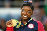 Simone Biles smiles as she holds a gold medal won at Rio 2016.