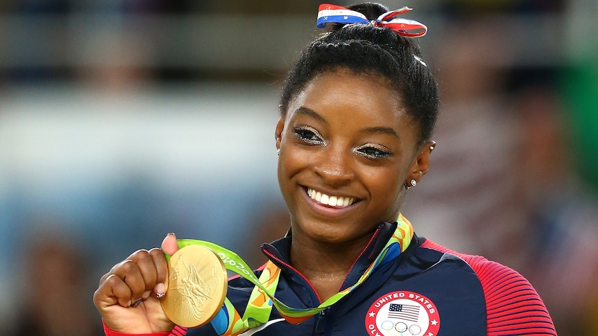 Simone Biles sorride mentre detiene una medaglia d'oro vinta a Rio 2016.