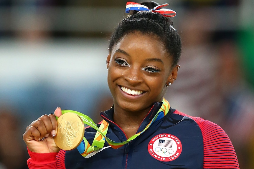 Simone Biles smiles as she holds a gold medal won at Rio 2016.