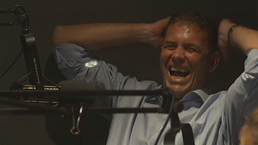 Dave Tollner in the studios of radio 104.9 Mix FM, laughing with his hands behind his head.