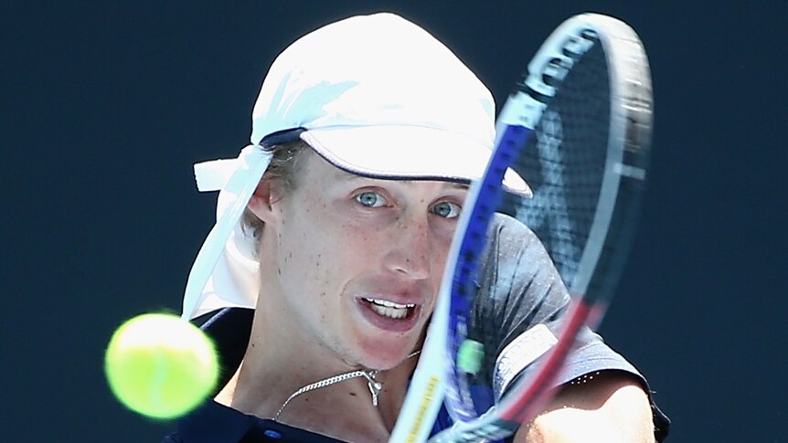 A male tennis player plays a double-handed backhand at the Australian Open as he watches the ball.
