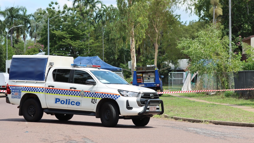 A NT Police vehicle parked in a suburban street on a sunny day, with police tape in the background.