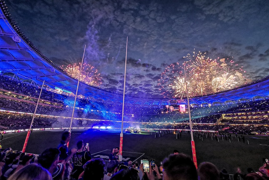 A photo of fireworks at dusk at Perth Stadium with blue lights in the background. 