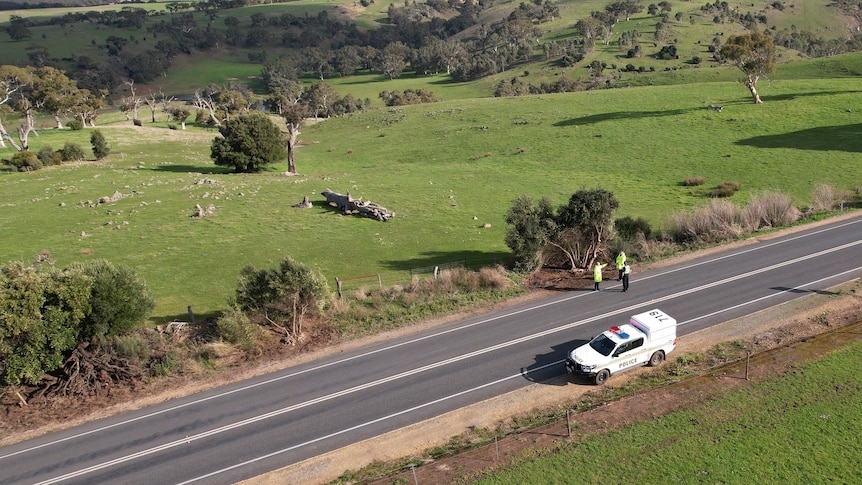 A drone image of a road with three police officers standing to the side and a police car on the opposite side