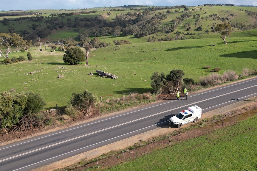 A drone image of a road with three police officers standing to the side and a police car on the opposite side
