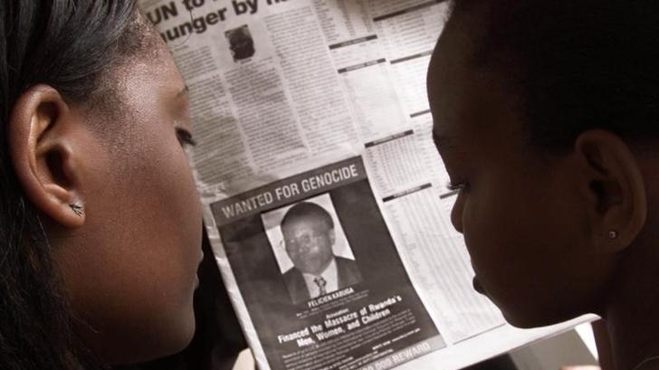 Two women looking at a newspaper add that shows a wanted picture of Felicien Kabuga.