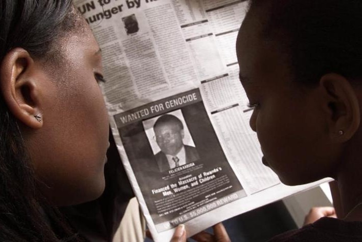 Two women looking at a newspaper add that shows a wanted picture of Felicien Kabuga.