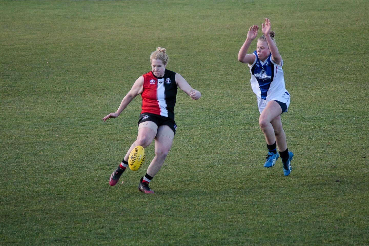 A player kicks the ball while another one tries to smother it.