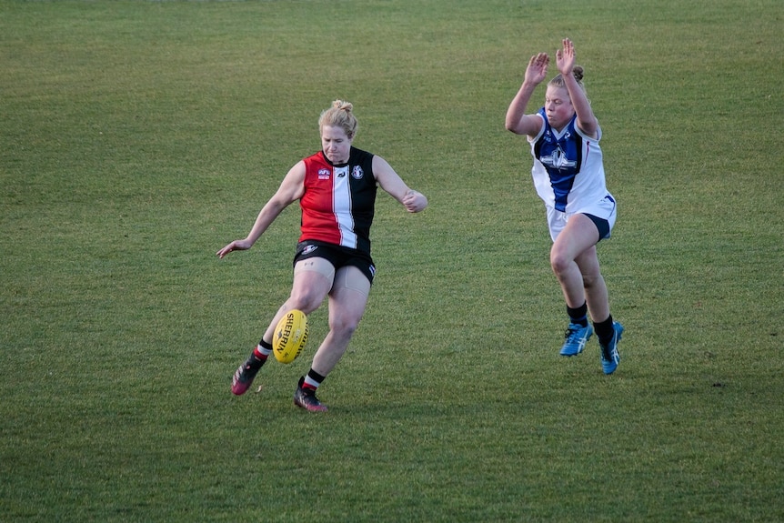 A player kicks the ball while another one tries to smother it.