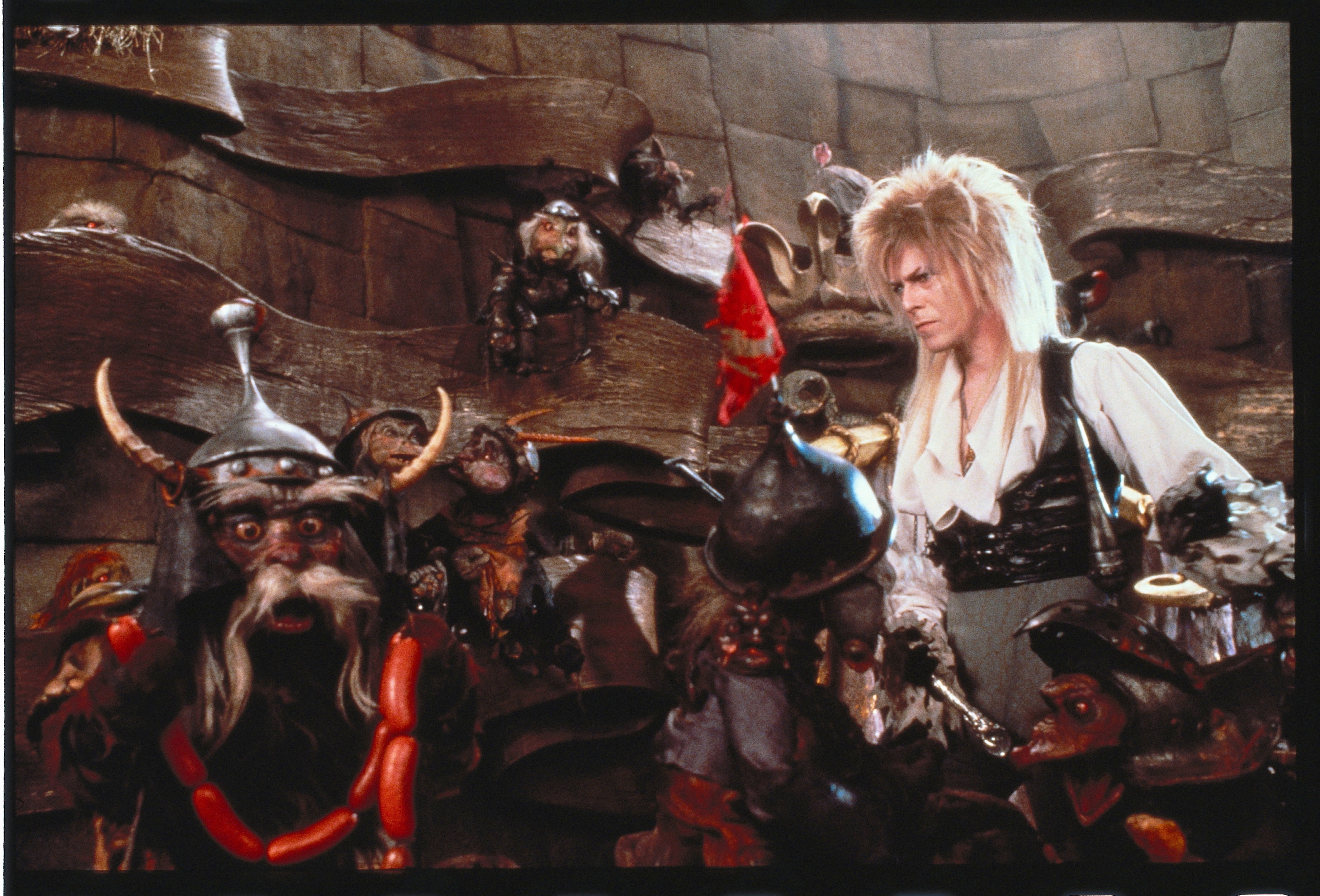 david bowie stands with goblin puppets in a scene from labyrinth