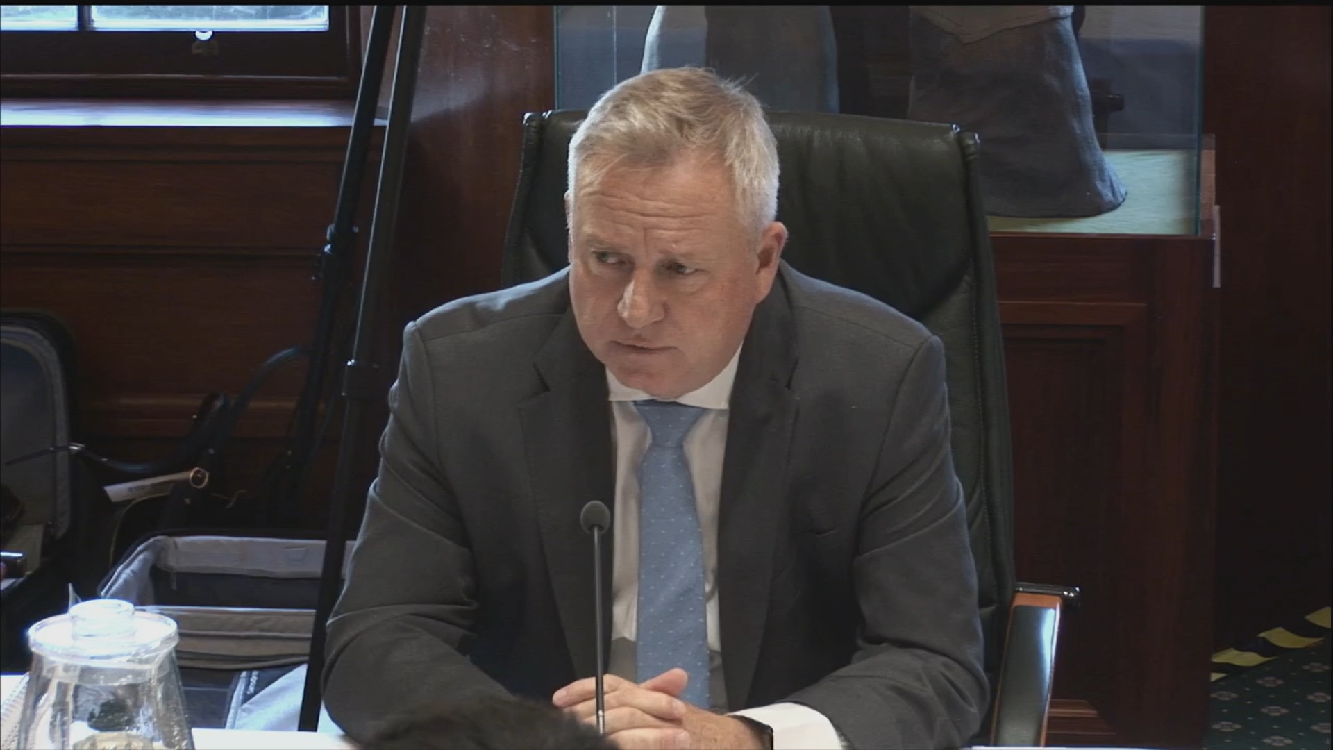 Jeremy, a middle aged man in a grey suit sits in front of a small microphone.