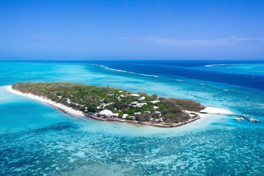 An oval shaped island with white sand beaches, greenery and coral reefs surrounding.