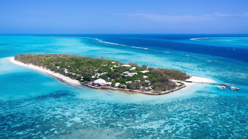 An oval shaped island with white sand beaches, greenery and coral reefs surrounding.